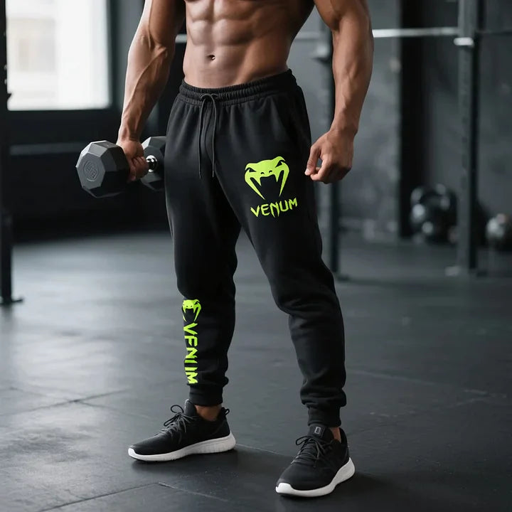 Mężczyzna muskularny w spodniach OVERSIZED Venu Lime czarnych, trzymający hantlę. Bawełna spieniona do fitnessu.